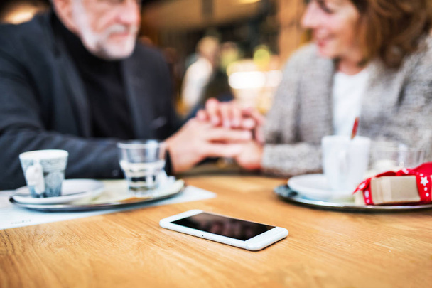 Senior couple with a smartphone in a cafe. Christmas time. - Zdjęcie, obraz