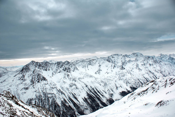 View of the mountains covered with snow and the cloudy low sky. - Photo, Image