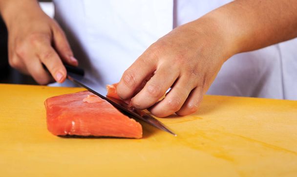 Giovane donna chef coock vestita in uniforme bianca tagliare il pesce salmone sul tavolo in cucina ristorante
 - Foto, immagini