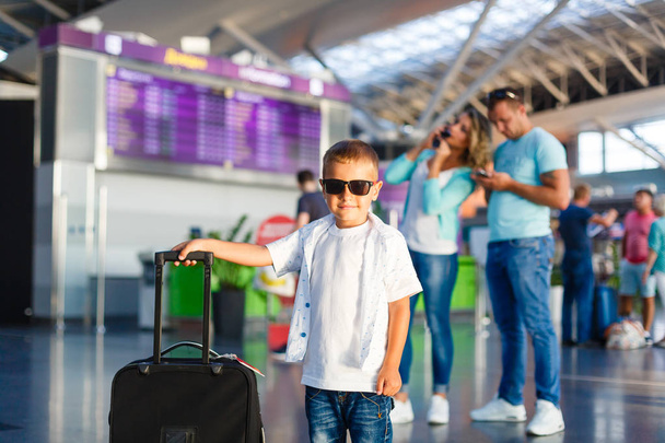 Χαριτωμένο μικρό αγόρι με βαλίτσα στέκεται με τους γονείς τους στην αίθουσα αεροδρομίου - Φωτογραφία, εικόνα
