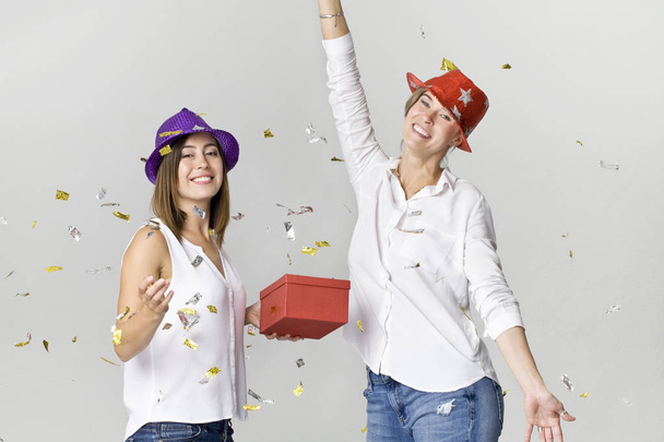 Party girlfriends with confetti, gift and colorful hats. It is relaxation and dancing time - Photo, Image