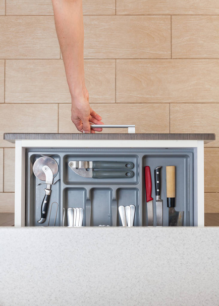High angle top view vertical photo of cropped woman hand open new kitchen drawer by modern door handle, with different cutlery spoon, pizza knife, fork and stuff - Photo, Image