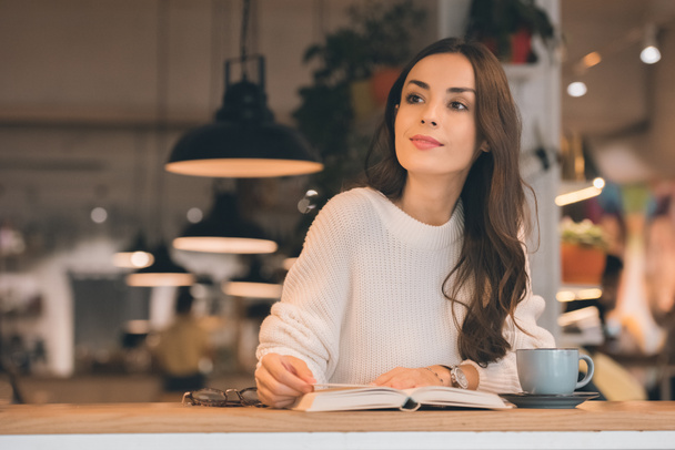 привлекательная женщина читает книгу за столом с чашкой кофе в кафе
 - Фото, изображение