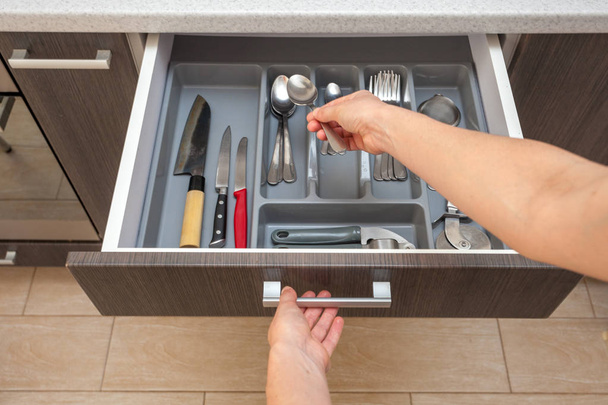 Leisure, lifestyle, domestic life concept. Photo from first person pov view woman hand open new brown kitchen drawer by modern door handle, with different cutlery take spoon to prepare dish food eat - 写真・画像