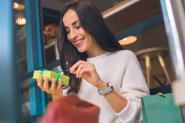 улыбающаяся молодая женщина развязывает подарочную коробку в кафе
 - Фото, изображение