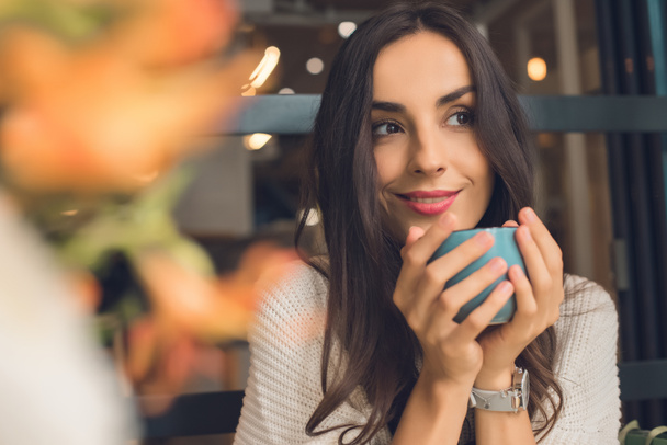 Selektywny fokus ładna kobieta trzymając kubek kawy przy stoliku w kawiarni  - Zdjęcie, obraz