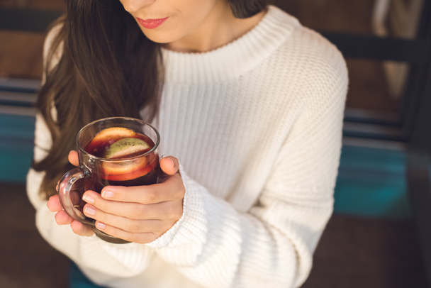 vista parcial de la joven mujer sosteniendo la taza de vino caliente en la mesa en la cafetería
 - Foto, imagen