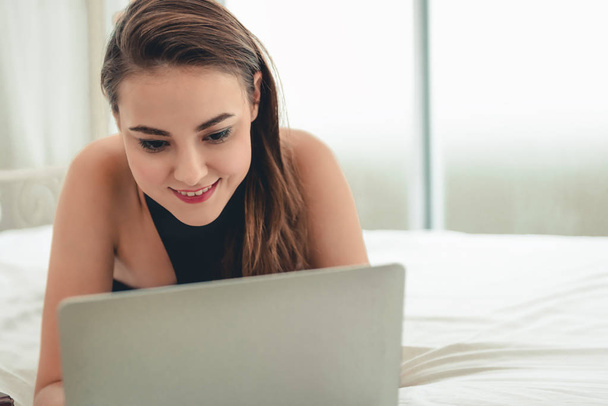 Retrato de una hermosa mujer acostada en su dormitorio mientras usa una computadora portátil
. - Foto, Imagen