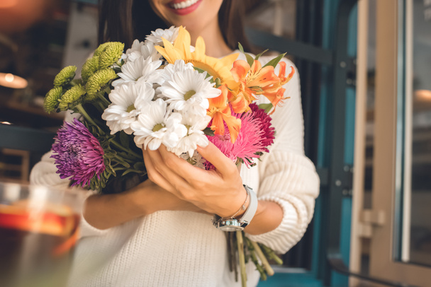 partial view of smiling young woman holding colorful bouquet from various flowers in cafe - Photo, Image