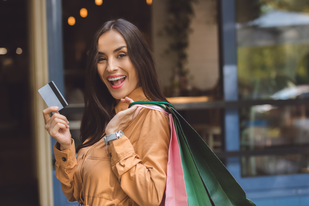 beautiful smiling woman with shopping bags showing credit card at city street - Photo, Image