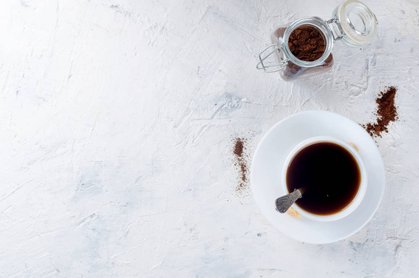 white cup of coffee and a glass jar with coffee powder on white concrete background, copy space, top view - Foto, imagen