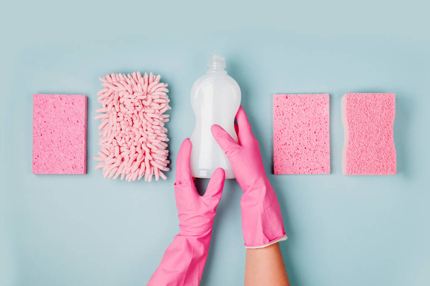 hands in pink rubber gloves holding bottle of cleanser with microfiber cloth and sponges - Fotó, kép