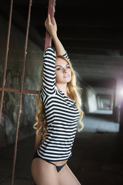 Sexy young blond woman in striped blouse posing near iron fence  - Фото, зображення
