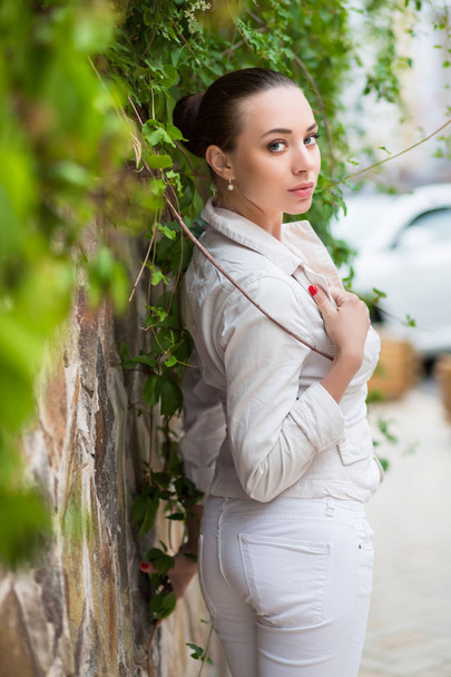 白いズボンとジャケットを屋外でポーズの若い女性 - 写真・画像