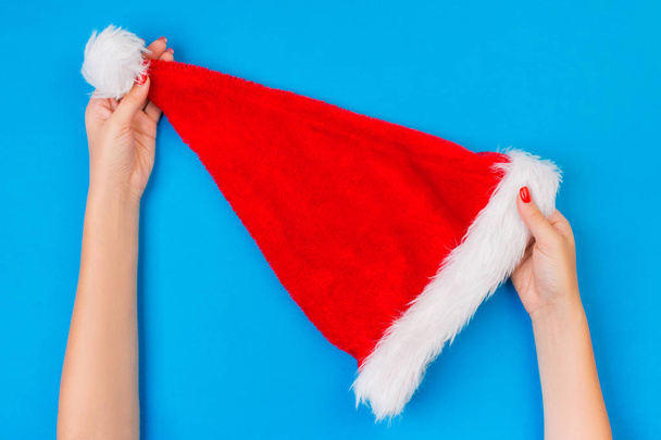 Девушка держать в руке Санта-Клауса красная шляпа на синем фоне, вид сверху
. - Фото, изображение