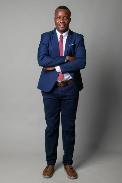 Ganzkörperaufnahme eines jungen glücklichen afrikanischen Geschäftsmannes im blauen Anzug - Foto, Bild