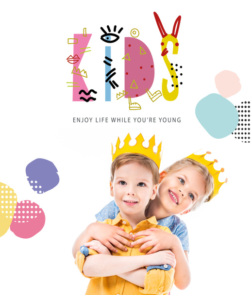 sister hugging brother, kids in yellow paper crowns, isolated on white with "kids - enjoy life while you are young" lettering - Photo, Image