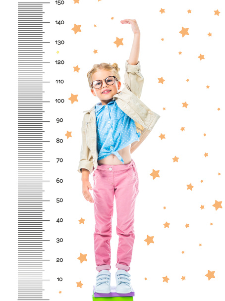 glückliches Kind mit Brille, das auf Bücherstapel steht, um höher isoliert auf weiß mit Sternen und Wachstumsmaßen zu sein - Foto, Bild