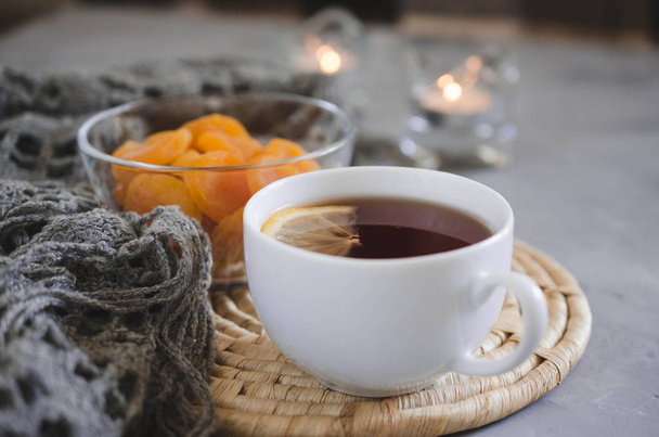 Stilleven details in het interieur van de woonkamer. Kopje thee en gedroogde abrikozen op een tafel, kaarsen en gebreide deken. Gezellige stemming herfst of winter in een lui weekend . - Foto, afbeelding