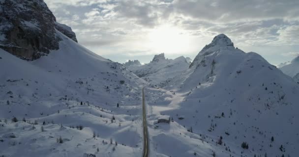 Aérea hacia adelante a lo largo de la carretera en el valle nevado en el paso Valparola. Soleado atardecer o amanecer, cielo nublado, sol retroiluminado.
. - Metraje, vídeo