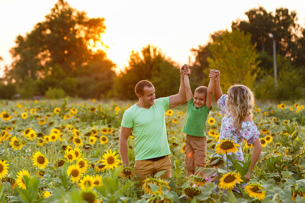 prachtige familie heeft een zoontje in een zonnebloem veld. tederheid, glimlach, geluk - Foto, afbeelding