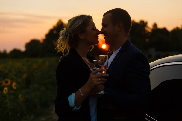 romantikus pár a naplemente intelligens alkalmi ruhában gazdaság szemüveg iszik pezsgőt - Fotó, kép