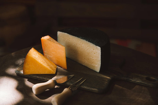 varios tipos de queso y cubiertos en la mesa de madera rústica
 - Foto, Imagen