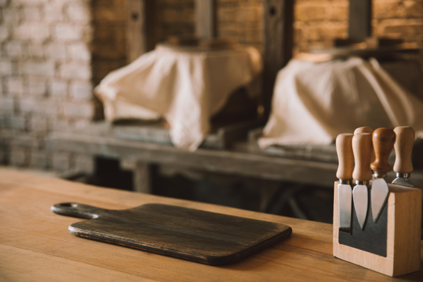 placa de corte vazia com facas de queijo no suporte na mesa de madeira na fabricação de queijo
 - Foto, Imagem