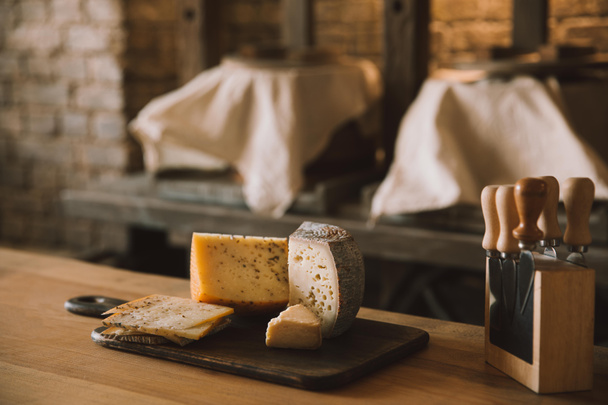крупним планом знімок смачного нарізаного сиру на дошці з різними ножами на підставці
 - Фото, зображення