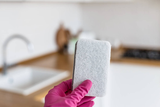 Woman hands wearing protective gloves and holding cleaning sponge on white kitchen background. Concept of clean kitchen - Photo, Image