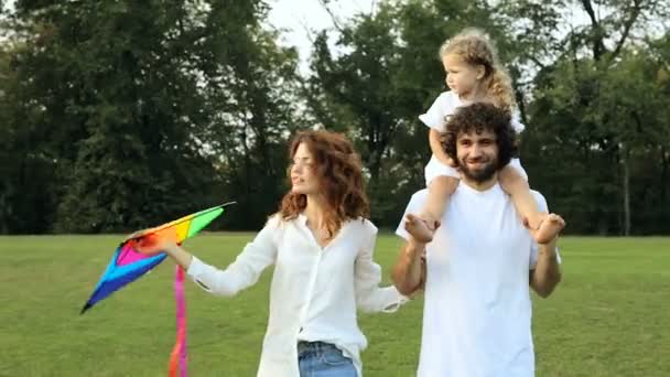 Happy family walking in the park together. Kid girl holding kite and sitting on the fathers shoulders. - Πλάνα, βίντεο