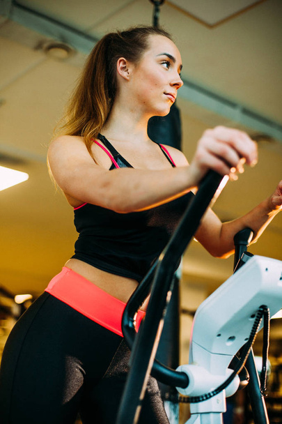 Jonge aantrekkelijke vrouw doet cardiotraining in de sportschool. - Foto, afbeelding