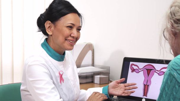 Жінка-гінеколог розмовляє зі своїм пацієнтом, показуючи матку на ноутбуці
 - Фото, зображення