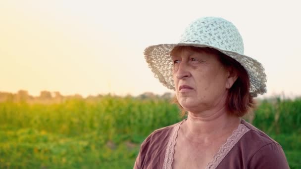Portret starszą kobietę życia na wsi. Dorosła kobieta ma na sobie biały kapelusz, ciesząc się widokiem w polu o zachodzie słońca - Materiał filmowy, wideo