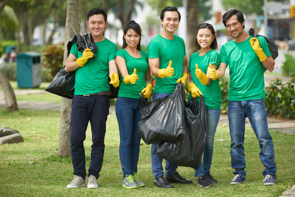 Team van jonge Vietnamese vrijwilligers tonen thumbs-up na het schoonmaken van park, mensen houden van vuilniszakken  - Foto, afbeelding