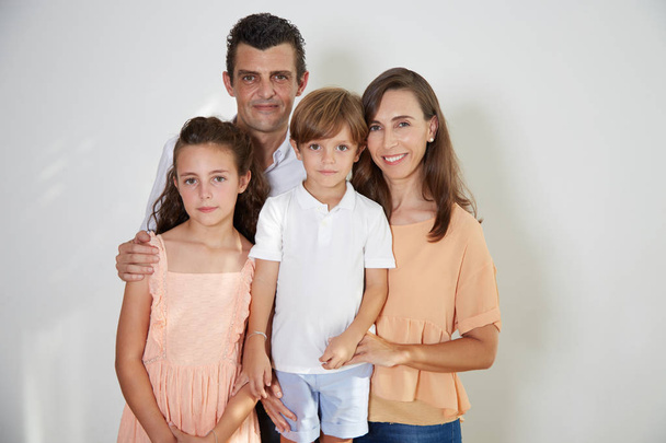 Happy family of four: mother, father, son and daughter posing in studio and looking at camera  - Фото, изображение