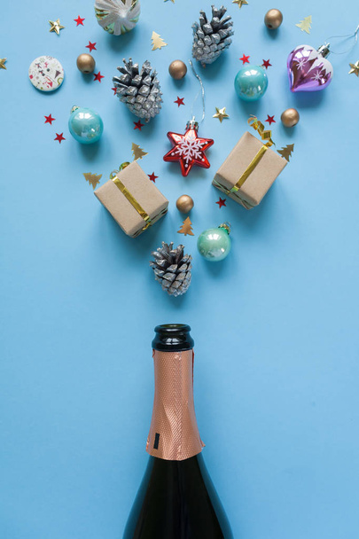 Champagne bottle with different christmas decoration on blue background. Open champagne concept. Flat lay. - Fotografie, Obrázek