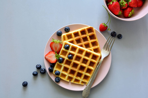 Belgian waffles with strawberries and blueberries on pink plate on gray wooden background. Top view. Copy space - Valokuva, kuva