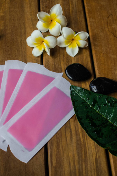 Pink cold wax strips on wooden surface with plumeria flowers and round black stones - Photo, Image