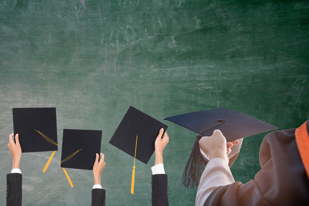 Graduation holds a black hat and a yellow tassel,The backdrop is a blackboard. - Valokuva, kuva