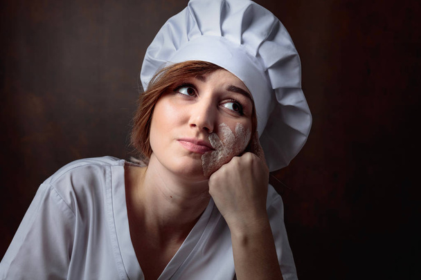 Unavený krásná mladá dívka v kuchař jednotný na hnědé zázemí. - Fotografie, Obrázek