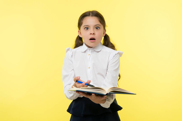 Girl cute schoolgirl in uniform hold book with information yellow background. Pupil get information from book. Child wear school uniform prepare for lesson information. Surprised about information - Foto, Imagen