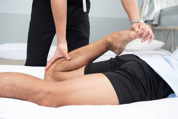 Fyzioterapeuty pomocí úchytů v pacienta nohy ležet na posteli v lékařské místnosti. - Fotografie, Obrázek