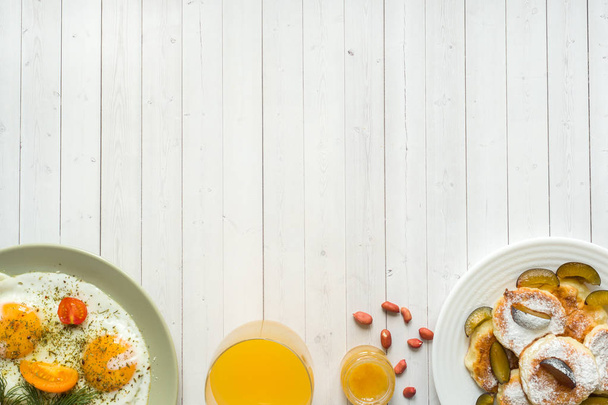 Concept of Breakfast. Fried eggs, cottage cheese pancakes, plums and oatmeal with milk, orange juice on the table. - Fotografie, Obrázek