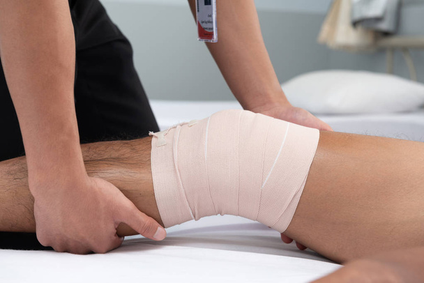 Les physiothérapeutes utilisent les poignées de la jambe du patient pour s'allonger sur le lit dans une salle médicale.
. - Photo, image