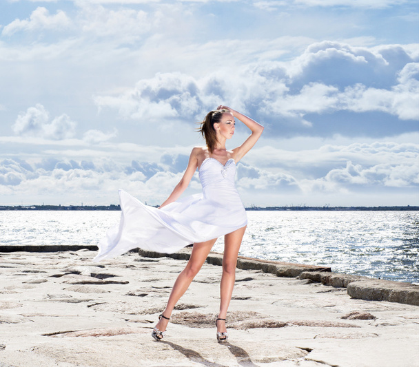 Young sexy girl in a white dress standing on a pier - Foto, Imagen