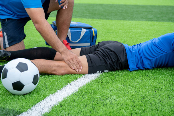 Fußballer trägt blaues Hemd, schwarze Hose verletzt sich während des Rennens auf dem Rasen. - Foto, Bild