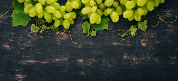 Fresh green grapes with leaves of grapes. Top view. On a black wooden background. Free space for text. - Valokuva, kuva