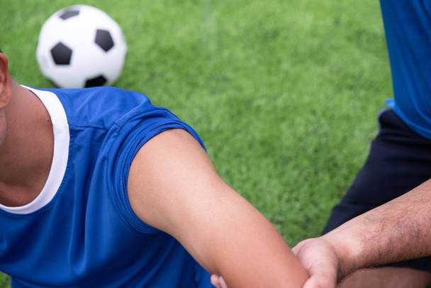 Ποδοσφαιριστής φοράει μπλε πουκάμισο, μαύρο παντελόνι τραυματίες στην του γκαζόν κατά τη διάρκεια του αγώνα. - Φωτογραφία, εικόνα