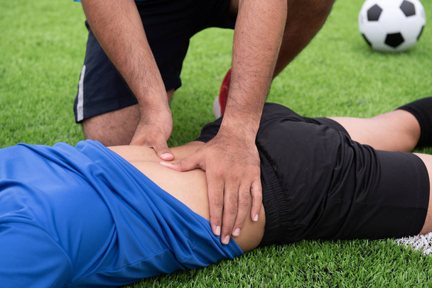 Fotbalista na sobě modrou košili, černé kalhoty, zraněn v trávníku během závodu. - Fotografie, Obrázek